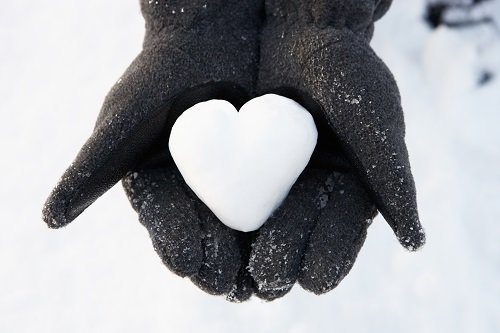 heart made out of snow in gloved hands